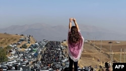 FILE - This UGC image posted on Twitter on Oct. 26, 2022, shows an unveiled woman standing atop a vehicle as thousands reportedly make their way toward the hometown of Mahsa Amini to mark 40 days since her death.