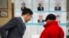 A member of the election commission, left, speaks to a voter in front of an election poster with photos and biographies of presidential candidates at a polling station in Almaty, Kazakhstan, Nov. 20, 2022. President Kassym-Jomart Tokayev is pictured in the bottom row, center.