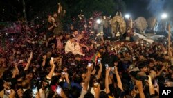 Pendukung Imran Khan melemparkan kelopak mawar ke arah kendaraan yang membawa mantan perdana menteri Pakistan itu untuk menyambut kedatangannya di rumahnya di Lahore, Pakistan, 13 Mei 2023. (Foto: AP)