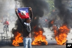 Seorang pengunjuk rasa mengibarkan bendera Haiti saat protes menuntut pengunduran diri Perdana Menteri Ariel Henry di Port-au-Prince, Haiti, Jumat, 1 Maret 2024. (Foto: AP)
