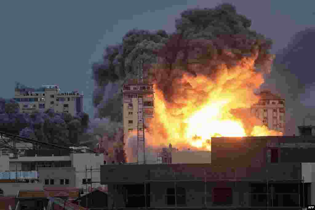 People standing on a rooftop watch as a ball of fire and smoke rises above a building in Gaza City on Oct. 7, 2023 during an Israeli airstrike that hit the Palestine Tower building. 