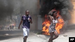 Demonstrators run past tires set on fire during a protest against insecurity in Port-au-Prince, Haiti, Aug. 7, 2023. 