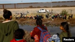 FILE - Migrants seeking asylum in the United States gather on the banks of the Rio Bravo river, as the Texas National Guard blocks the crossing at the border between the U.S. and Mexico, as seen from Ciudad Juarez, Mexico, Dec. 5, 2023. 
