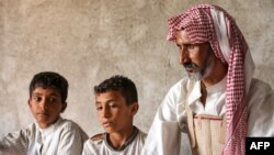 Nasser Jabbar bersama kedua anaknya duduk di rumah mereka yang terletak di pinggiran Kota Nasiriyah, provinsi Dhi Qar, Irak, pada 25 September 2023. (Foto: AFP/Asaad Niazi)