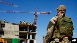 Seorang tentara Rusia tampak mengawasi pembangunan sebuah gedung apartemen baru di Mariupol, di wilayah Donetsk, Ukraina, yang kini dikuasai Rusia, pada 13 Juli 2022. Pembangunan tersebut didukung oleh Kementerian Pertahanan Rusia.(Foto: AP)
