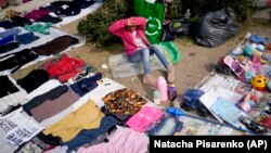A vendor sits surrounded by her secondhand garments at a market near Buenos Aires, Argentina, Wednesday, Aug. 10, 2022. (AP Photo/Natacha Pisarenko)