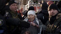 基辅一处居民楼遭到俄军轰击后，警察帮助一位消防队员从楼房中救出的老年妇女。(2022年3月15日)