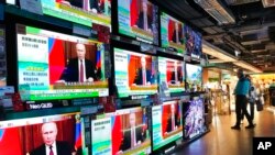 Tampak beberapa orang berdiri di dekat layar televisi yang menayangkan berita invasi Rusia ke Ukraina di sebuah pusat perbelanjaan di Hong Kong, pada 24 Februari 2022. (Foto: AP/Vincent Yu)