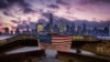 FILE - A U.S. flag hanging from a steel girder, damaged in the Sept. 11, 2001 attacks on the World Trade Center, blows in the breeze at a memorial in Jersey City, N.J., Sept. 11, 2019 as the sun rises behind One World Trade Center building in New York.