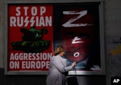 Seorang perempuan berjalan melewati dinding dengan poster yang menggambarkan Presiden Rusia Vladimir Putin, kanan, di Warsawa, Polandia, 24 Maret 2022. (Foto: AP)