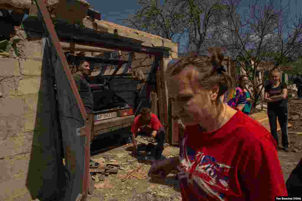 A family cleans up after a missile landed on their street in Zaporizhzhya. Three people were injured in this attack on April 28, 2022.