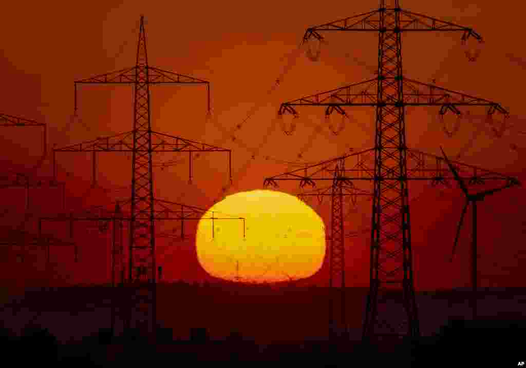 Almaniya - Frankfurt şəhəri ətrafında elektrik dirəklərinin arxasından günəşin çıxması görünür.