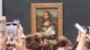 Los visitantes toman fotos y graban un video de la imagen de la "Mona Lisa", después de que hombre usara crema de pastel sobre el vidrio protector el Museo Lourve en París, Francia, el 29 de mayo de 2022 en esta captura de pantalla obtenida de un video de las redes sociales.
