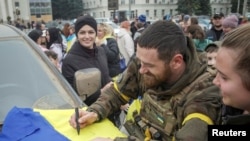 A Ukrainian serviceman writes on a Ukrainian national flag, an apparent keepsake for local residents, as people celebrate after Russia's retreat from Kherson city, in downtown Kherson, Ukraine Nov. 12, 2022.