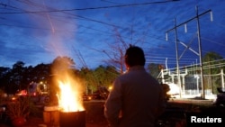 Gerardo Anicero warms himself in front of a makeshift fire as he watches Duke Energy personnel work to restore power at a crippled electrical substation that workers said was hit by gunfire, in Carthage, North Carolina, Dec. 4, 2022. 