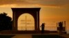 FILE - A woman uses her mobile phone to take a picture of her friend as the sun sets behind Saint Simon Church in Ghosta, in east Beirut, Lebanon, Oct. 8, 2022. 