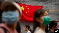 Orang-orang berjalan melewati bendera China di jalan perbelanjaan turis pada hari pertama periode liburan Hari Nasional di Beijing, 1 Oktober 2022. (Foto: AP)