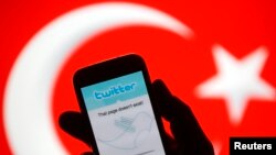 FILE - A person holds a mobile phone displaying a Twitter error message in front of Turkish national flag in this illustration taken in Zenica, March 21, 2014. 