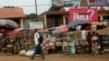 FILE – A sign urging precautions to fight the spread of Ebola hangs over a market in Guinea's capital, Conakry, Dec. 3, 2014. (Dominic Chavez/World Bank)