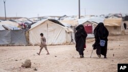 FILE - Women walk in the al-Hol camp that houses some 60,000 refugees, including families and supporters of the Islamic State group, many of them foreign nationals, in Hasakeh province, Syria, May 1, 2021. France said Tuesday it repatriated 25 children and 10 women from a camp.