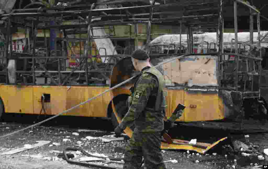 Seorang separatis pro-Rusia melewati bus yang hancur dalam pertempuran antara pemberontak pro-Rusia dan pasukan pemerintah di Donetsk, Ukraina timur (11/2). ​(AP/Petr David Josek)