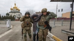 Dua prajurit Ukraina memapah seorang perempuan lansia di kota Irpin, Ukraina, Minggu, 6 Maret 2022. (AP Photo/Andriy Dubchak, File)