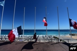 FILE - In this file photo taken on July 15, 2016, a woman sits under French flags lowered at half-mast in Nice, a day after Mohamed Lahouaiej-Bouhlel, a 31-year-old dual national, Tunisian-born, drove a truck through a crowd celebrating Bastille Day.