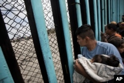 A member of the Central American migrant caravan, holding a child, looks through the border wall toward a group of people gathered on the U.S. side, as he stands on the beach where the border wall ends in the ocean, in Tijuana, Mexico, April 29, 2018.