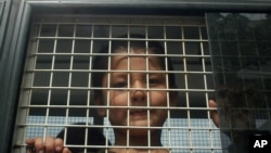 FILE - Ethnic Uighur Muslim boy stands inside a police van in Khlong Hoi Khong of southern Songkhla province, Thailand. He was in a group of 200 people rescued from a human trafficking camp.