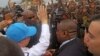 U.N. Secretary-General Ban Ki-moon, in a cap, waving at people kept back by a wire fence, as he walks surrounded by U.N. security personnel in a secured location in Bangui, Central African Republic, April 5, 2014.