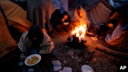 Migrants eat around a fire at a camp in Velika Kladusa, Bosnia, close to the border to Croatia, Nov. 18, 2018. 