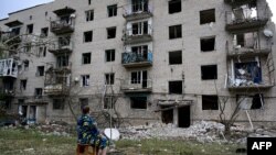 A woman sits in front of her building, which has been partialy destroyed after a Russian missile hit on a four-storey residential building in Chasiv Yar, Bakhmut District, eastern Ukraine, on July 10, 2022.