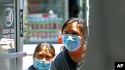 Two women peer into a clothing store to see if it is open, June 8, 2020, in the Sunset Park neighborhood of the Brooklyn borough of New York. 