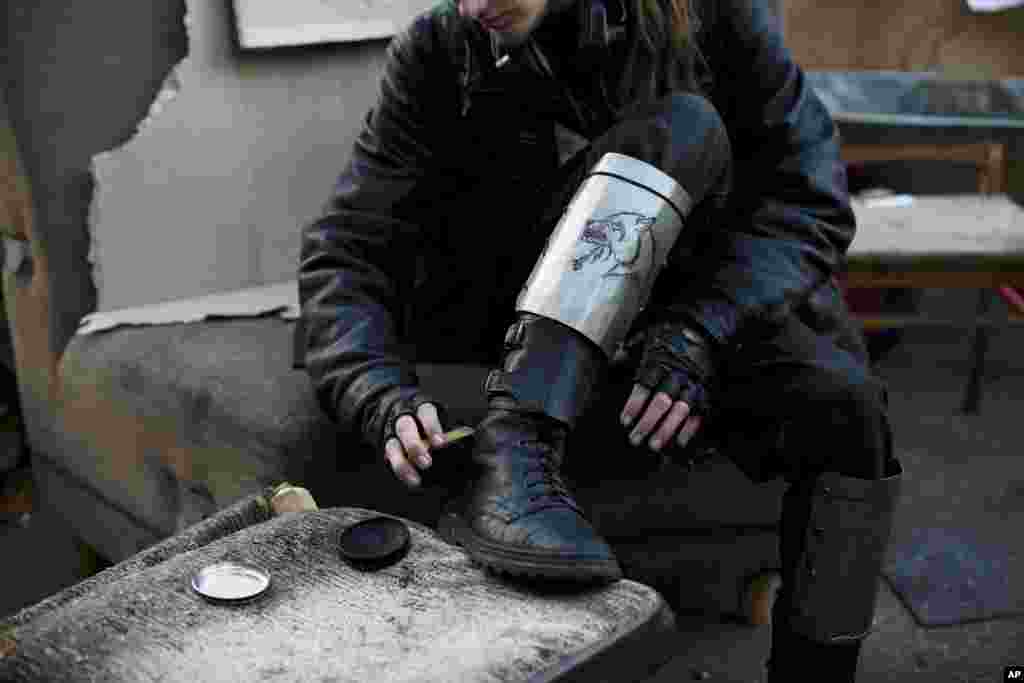 Seorang anggota kelompok relawan pertahanan diri, dengan pelindung tulang kering darurat bergambarkan serigala, menyemir sepatu boots miliknya di Lapangan Kemerdekaan Kyiv, Ukraina, 11 Maret 2014.&nbsp;