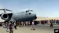 Hundreds of people run alongside a U.S. Air Force C-17 transport plane as it moves down a runway of the international airport, in Kabul, Afghanistan, Aug.16. 2021.