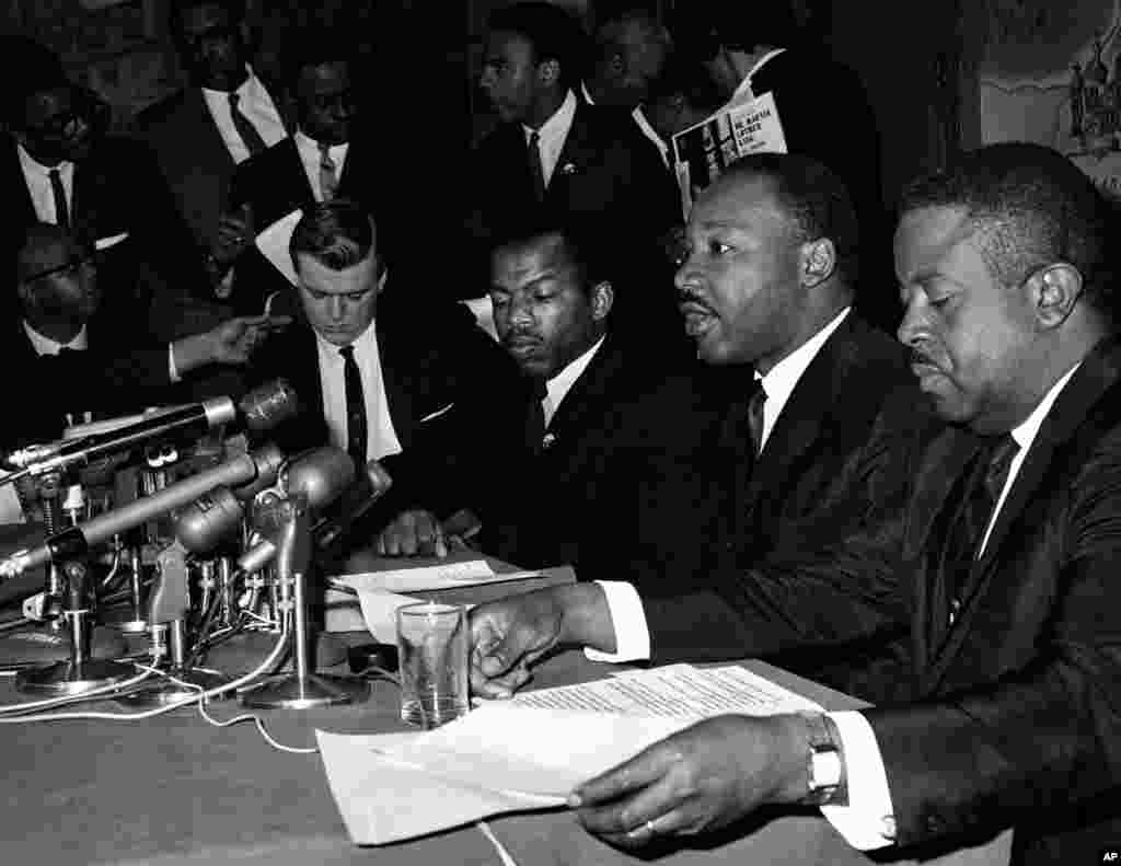លោក Martin Luther King, Jr. ថ្លែង​នៅ​ក្នុង​សន្និសីទ​កាសែត​មួយ​ នៅ​ក្បែរ​លោក John Lewis ដែល​ជា​ប្រធាន​នៃ​គណៈកម្មាធិការ​សម្របសម្រួល​អំពើ​អហិង្សា​របស់​និស្សិត​ នៅ​ក្នុង​ក្រុង Baltimore រដ្ឋ Maryland កាលពី​ថ្ងៃទី២ ខែមេសា ឆ្នាំ១៩៦៥។