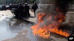 Riot police stand by an overthrown car during a demonstration by taxi drivers opposed to ride-sharing service Uber in Paris, June 25, 2015.