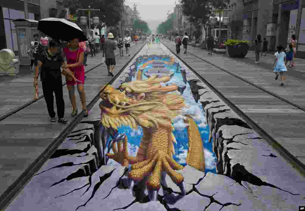 Chinese women look at a 3D painting of a dragon at Qianmen Street, a popular tourist spot in Beijing, China, August 11, 2013. 