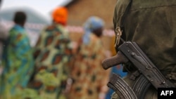 Un homme avec son arme en bandoulière regarde des femmes qui passent à Aveba, dans le sud de l’Ituri, RDC, 30 juillet 2006.