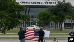 FILE - Men hold a sign and a U.S. flag across the street from the Curtis Culwell Center, where two men opened fire at an event soliciting cartoons of the Prophet Mohammad, in Garland, Texas, May 5, 2015.