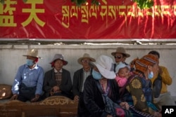 Ljudi odmaraju u hladu ispod vladinog propagandnog transparenta u tibetanskoj u četvrti Chengguan u Lhasi u Tibetu, zapadna Kina, 3. juna 2021.