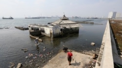 People walk near a giant sea wall that prevents sea water from flowing into Jakarta, Indonesia, July 27, 2019.