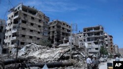 FILE - People stand in front of damaged buildings, in the town of Douma, the site of a suspected chemical weapon attack, near Damascus, Syria, on April 16, 2018. 
