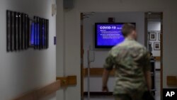 FILE - A member of the U.S. Army walks down the hall toward a monitor displaying COVID-19 safety information in Fort Meade, Md., March 25, 2020.