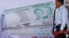Cambodian men stand near local and international currencies poster during an inauguration ceremony of the Cambodia Securities Exchange in Phnom Penh, file photo. 