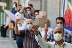 Pria Iran menunjukkan identitas mereka saat mereka mengantre untuk memilih presiden di sebuah tempat pemungutan suara di Teheran, pada 18 Juni 2021. (Foto: AFP/Atta Kenare)