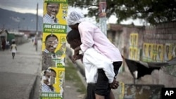 Man, carrying woman with cholera symptoms, walks past campaign posters showing presidential candidate Jude Celestin in Port-au-Prince, Haiti, 11 Nov., 2010.