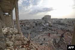 FILE - Syrians gather amidst destruction in Zardana, in the mostly rebel-held northern Syrian Idlib province, in the aftermath of air strikes in the area late on June 8, 2018.