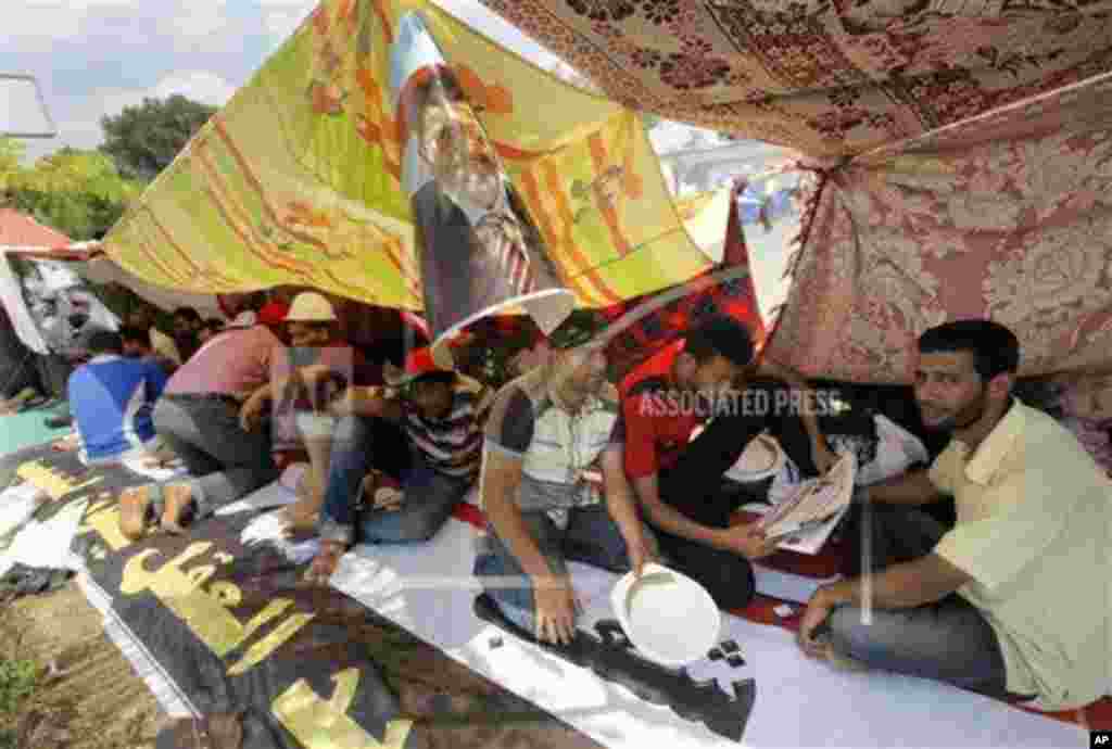Egyptian supporters of Egypt's Islamist President Mohammed Morsi read newspapers under his poster at their camp outside of the Rabia el-Adawiya mosque near the presidential palace, July 2, 2013.