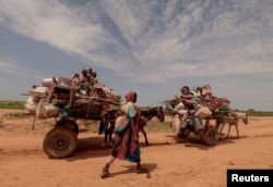 FILE - A Sudanese woman who fled the conflict in Sudan's Darfur region walks beside carts carrying her family belongings upon crossing the border between Sudan and Chad in Adre, Chad, on Aug. 2, 2023.